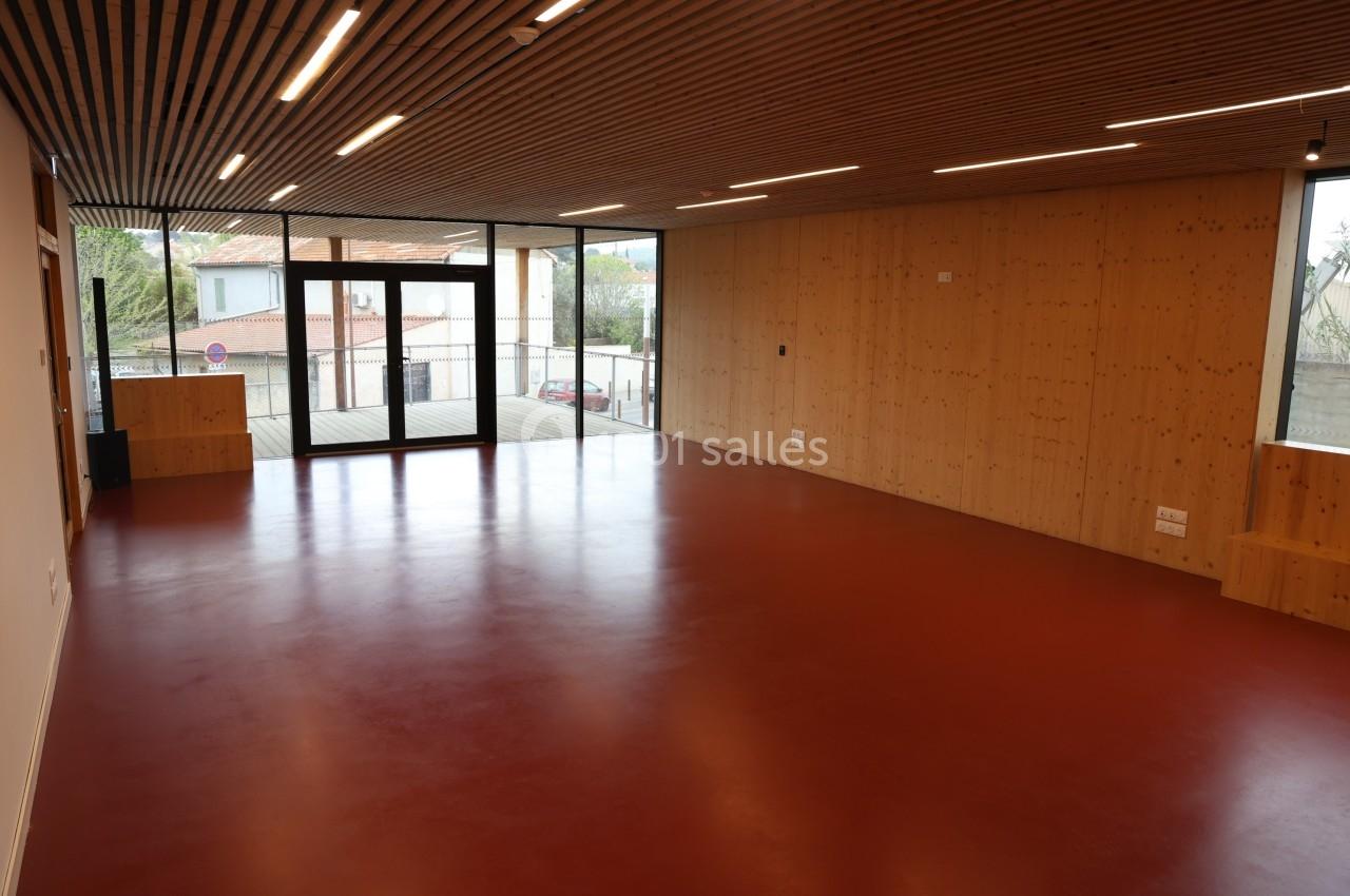 Salle vide avec sol rouge, murs en bois clair, plafond à lattes et grandes baies vitrées donnant sur l'extérieur.