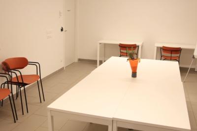 Salle de réunion lumineuse avec tables blanches, chaises orange et un tableau blanc sur pied.
