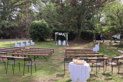 Salon avec téléviseur, fauteuils blancs, chaise orange, tapis à motifs et vue partielle sur une cuisine ouverte.