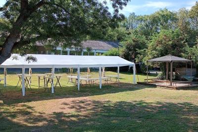 Salon avec téléviseur, fauteuils blancs, chaise orange, tapis à motifs et vue partielle sur une cuisine ouverte.
