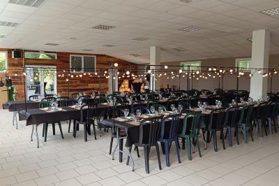 Salon avec téléviseur, fauteuils blancs, chaise orange, tapis à motifs et vue partielle sur une cuisine ouverte.
