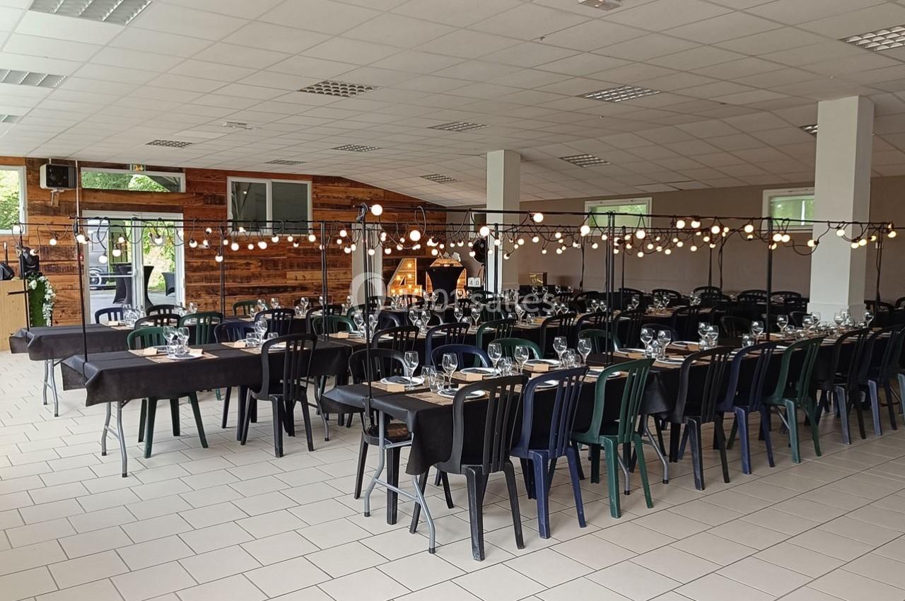Salle décorée pour un événement, avec des tables dressées, des chaises colorées et des guirlandes lumineuses suspendues.