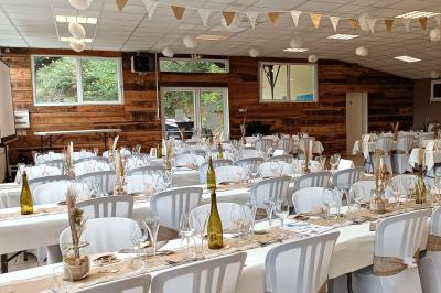 Salon avec téléviseur, fauteuils blancs, chaise orange, tapis à motifs et vue partielle sur une cuisine ouverte.