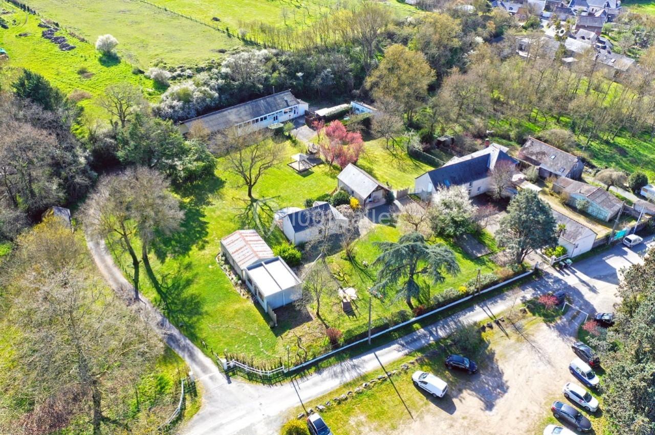 Vue aérienne d'un ensemble de bâtiments ruraux entourés de jardins, d'arbres et de prairies verdoyantes.