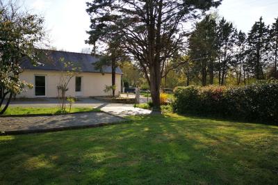 Salon avec téléviseur, fauteuils blancs, chaise orange, tapis à motifs et vue partielle sur une cuisine ouverte.