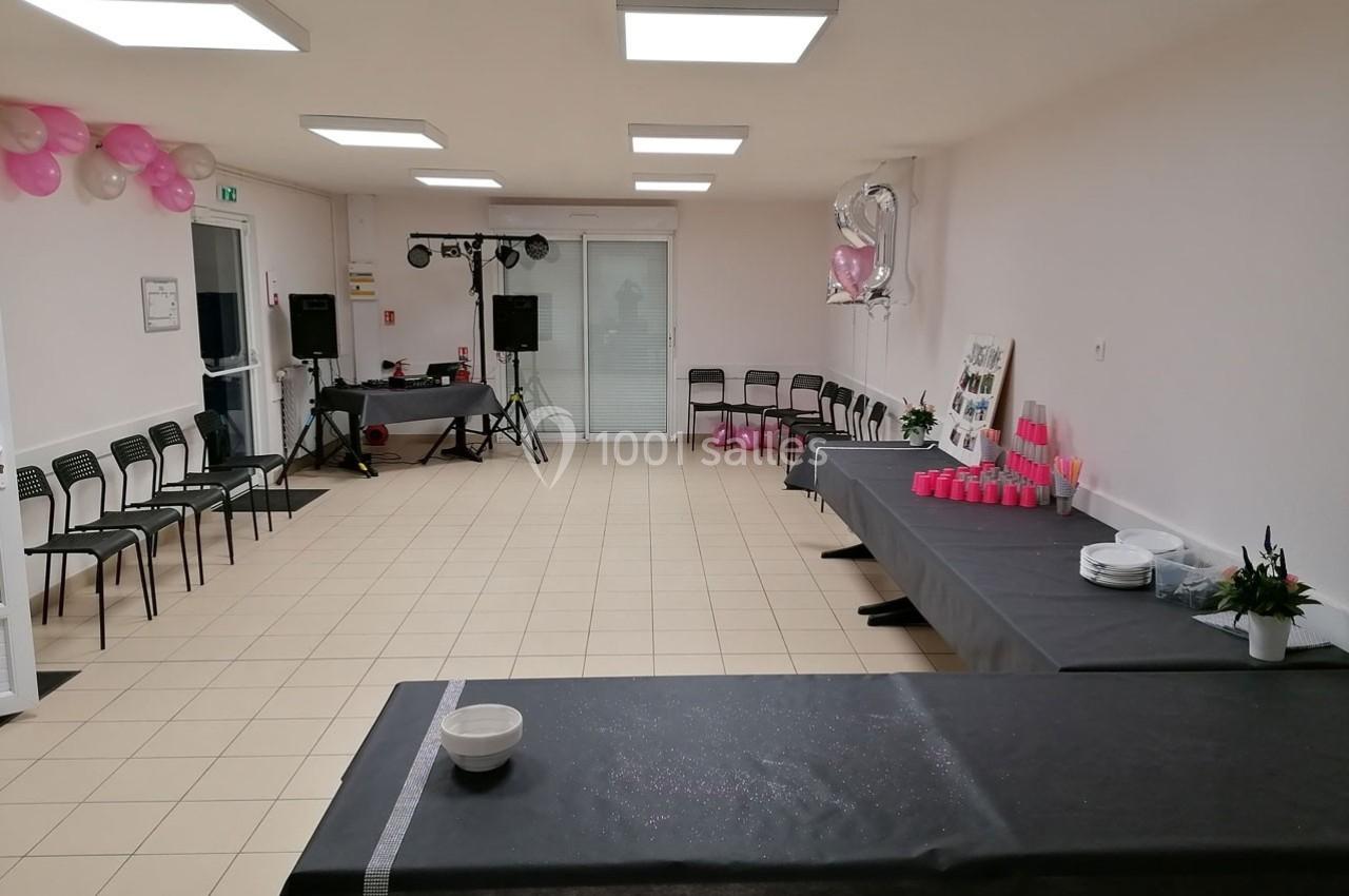 Salle décorée pour un événement avec tables recouvertes de nappes noires, chaises alignées et ballons roses.