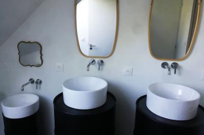 Salon avec téléviseur, fauteuils blancs, chaise orange, tapis à motifs et vue partielle sur une cuisine ouverte.