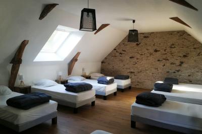 Salon avec téléviseur, fauteuils blancs, chaise orange, tapis à motifs et vue partielle sur une cuisine ouverte.