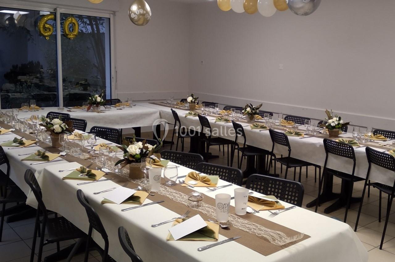 Salle décorée pour une réception avec tables dressées, nappes blanches, décorations dorées et bouquets de fleurs.