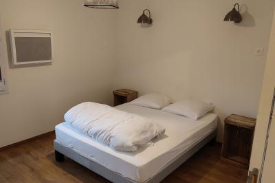 Salon avec téléviseur, fauteuils blancs, chaise orange, tapis à motifs et vue partielle sur une cuisine ouverte.