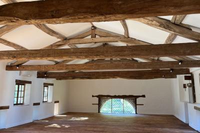 Salle rustique avec murs en pierre, poutres apparentes, table dressée, chaises en bois et coin salon avec canapé.