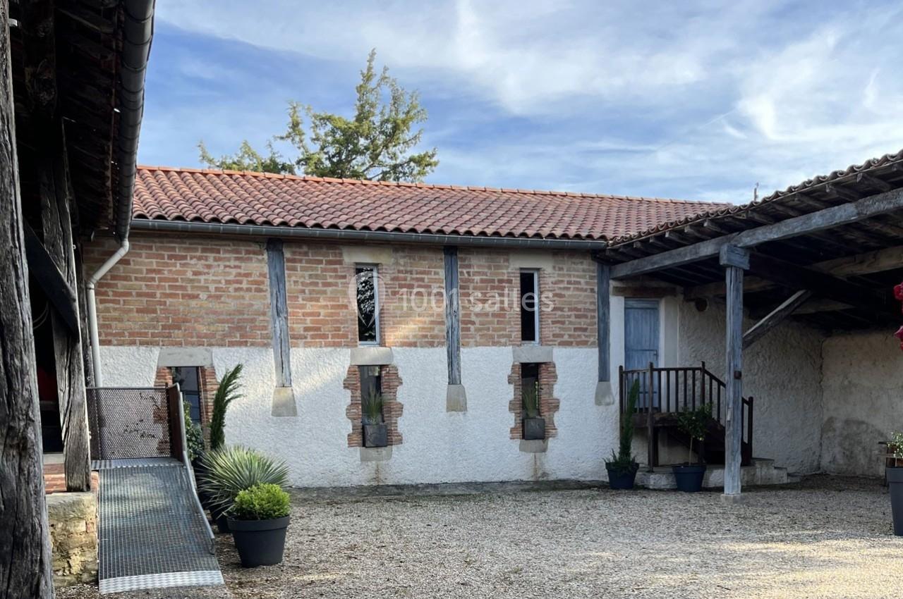 Cour intérieure avec bâtiment en briques et crépi, toit en tuiles rouges, rampe d'accès et plantes en pots.