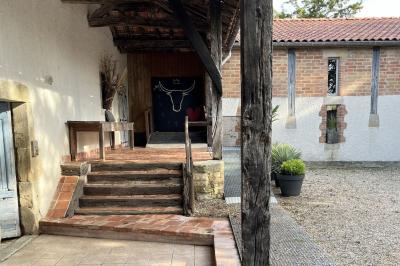 Salle rustique avec murs en pierre, poutres apparentes, table dressée, chaises en bois et coin salon avec canapé.