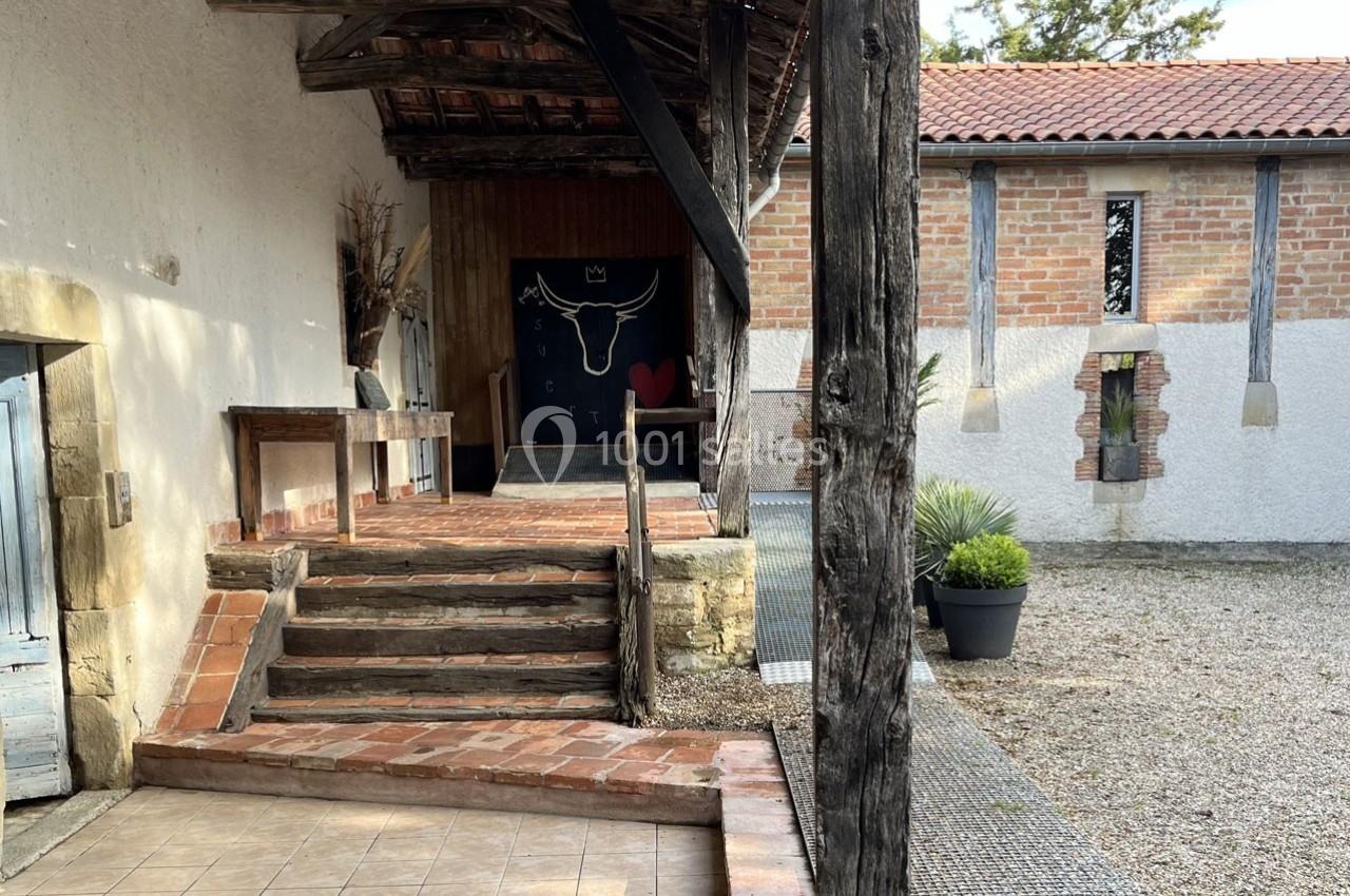 Entrée d'un bâtiment rustique avec murs en pierre, escalier en briques et porte ornée d'un dessin de taureau.