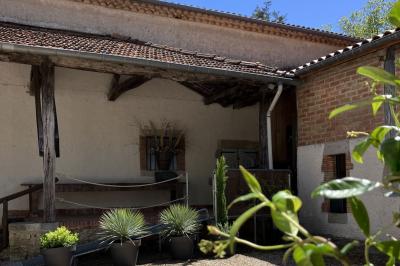 Salle rustique avec murs en pierre, poutres apparentes, table dressée, chaises en bois et coin salon avec canapé.