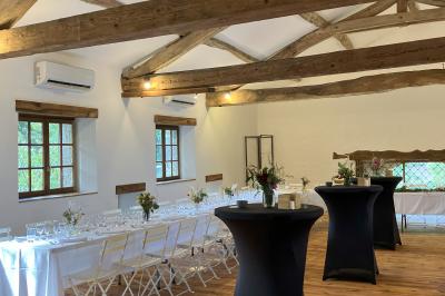 Salle rustique avec murs en pierre, poutres apparentes, table dressée, chaises en bois et coin salon avec canapé.