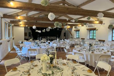 Salle rustique avec murs en pierre, poutres apparentes, table dressée, chaises en bois et coin salon avec canapé.