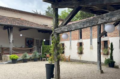 Salle rustique avec murs en pierre, poutres apparentes, table dressée, chaises en bois et coin salon avec canapé.