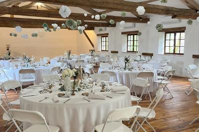 Salle rustique avec murs en pierre, poutres apparentes, table dressée, chaises en bois et coin salon avec canapé.