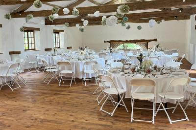 Salle rustique avec murs en pierre, poutres apparentes, table dressée, chaises en bois et coin salon avec canapé.
