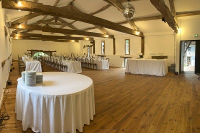 Salle rustique avec murs en pierre, poutres apparentes, table dressée, chaises en bois et coin salon avec canapé.