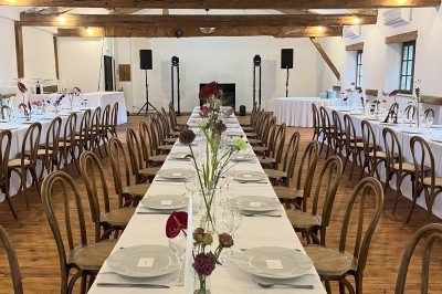 Salle rustique avec murs en pierre, poutres apparentes, table dressée, chaises en bois et coin salon avec canapé.