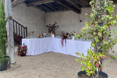 Salle rustique avec murs en pierre, poutres apparentes, table dressée, chaises en bois et coin salon avec canapé.