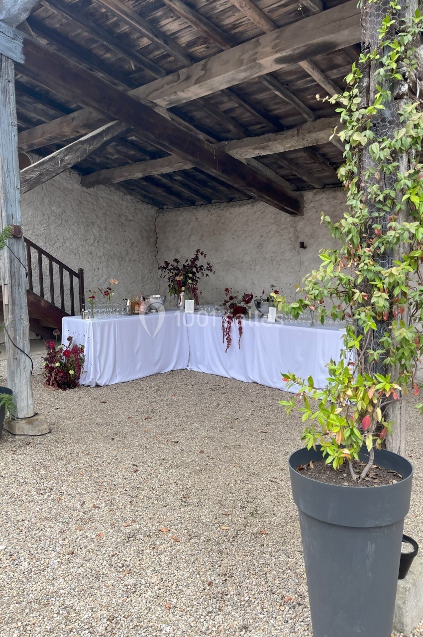 Table de buffet décorée avec des nappes blanches et des arrangements floraux, installée sous un abri en bois.