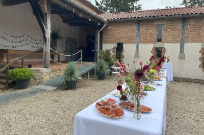 Salle rustique avec murs en pierre, poutres apparentes, table dressée, chaises en bois et coin salon avec canapé.