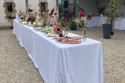 Salle rustique avec murs en pierre, poutres apparentes, table dressée, chaises en bois et coin salon avec canapé.