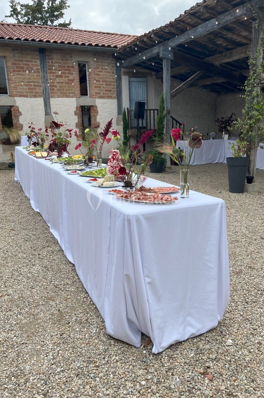 Table de buffet décorée de fleurs rouges et blanches, dressée en extérieur sous un auvent dans une cour en gravier.