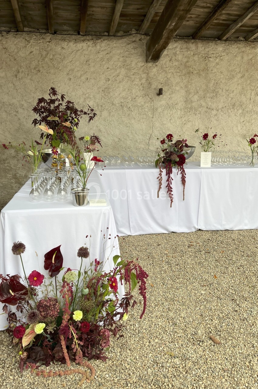 Tables décorées de nappes blanches avec arrangements floraux rouges et verts, installées sur un sol en gravier.