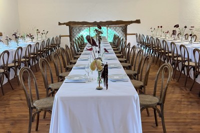 Salle rustique avec murs en pierre, poutres apparentes, table dressée, chaises en bois et coin salon avec canapé.