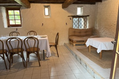 Salle rustique avec murs en pierre, poutres apparentes, table dressée, chaises en bois et coin salon avec canapé.