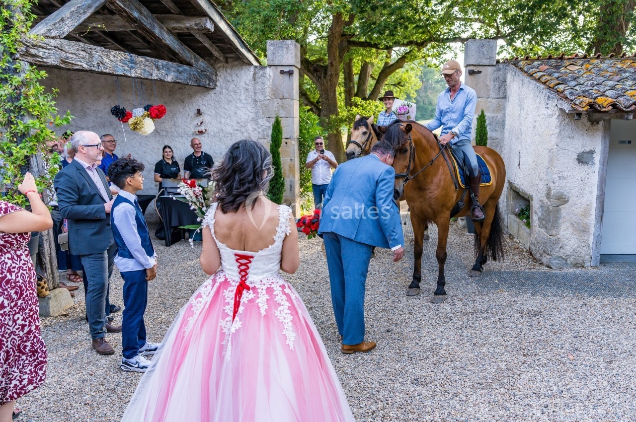Un homme à cheval salue un groupe de personnes lors d'un événement en extérieur, avec une mariée au premier plan.