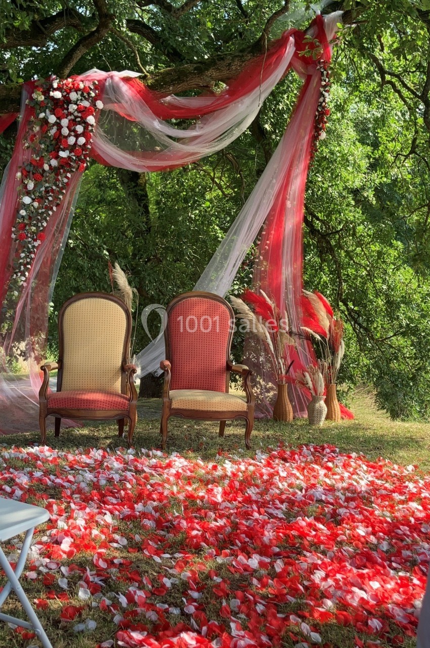 Deux fauteuils anciens sous une arche décorée de fleurs rouges et blanches, avec des pétales éparpillés au sol.