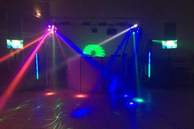 Des couples dansent sous des jeux de lumière colorés dans une salle sombre, créant une ambiance festive.
