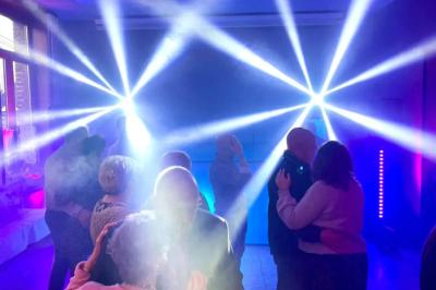 Des couples dansent sous des jeux de lumière colorés dans une salle sombre, créant une ambiance festive.