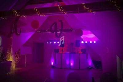 Salle de réception décorée avec des lumières violettes, guirlandes lumineuses et une piste de danse équipée de matériel DJ.