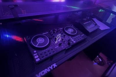 Table de mixage DJ avec platines et contrôleurs éclairés par des lumières colorées dans un environnement sombre.