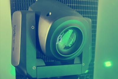 Projecteur lumineux motorisé avec lentille visible, entouré d'une lumière verte diffuse.