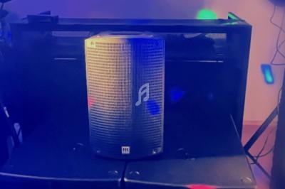 Haut-parleur noir posé sur une enceinte, éclairé par des lumières colorées dans un environnement sombre.