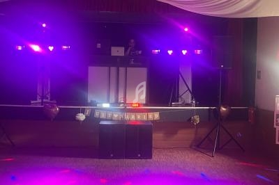 Un DJ anime une soirée dans une salle décorée avec des lumières colorées et une bannière ’Just Married’.