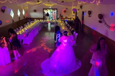 Salle de réception décorée avec des guirlandes lumineuses, tables dressées en U et invités en tenue de cérémonie.