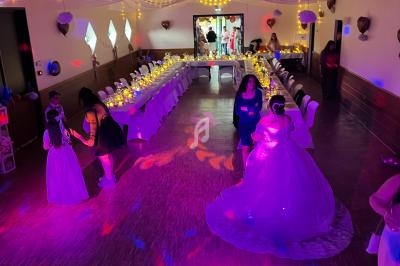 Salle décorée pour une fête, avec des invités dansant sous des lumières colorées et des tables dressées en arrière-plan.