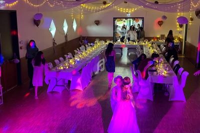 Salle décorée pour une réception avec des tables dressées, des guirlandes lumineuses et des invités en arrière-plan.