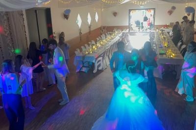 Des invités dansent dans une salle décorée pour une réception, avec des tables dressées et des lumières colorées.