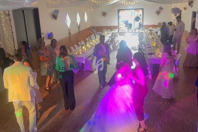 Personnes dansant dans une salle décorée pour un mariage, avec tables dressées et lumières colorées.