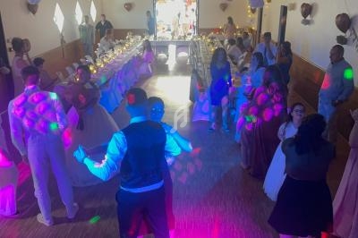 Des invités dansent dans une salle décorée pour une réception, avec des lumières colorées et des tables dressées en arrière…