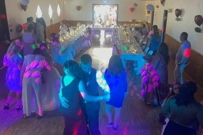 Personnes dansant sur une piste éclairée de lumières colorées, avec une table de réception décorée en arrière-plan.